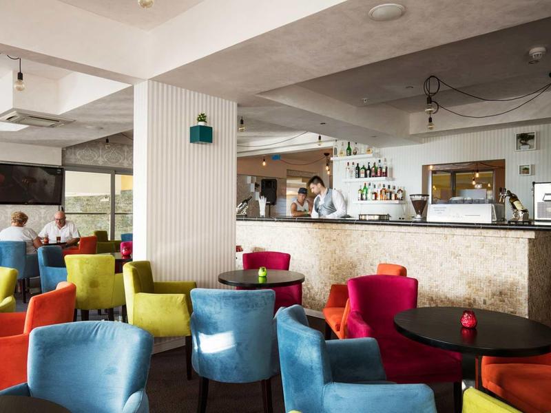Heller Caféraum mit bunten Sesseln, schwarzen Tischen und hellem Bartresen im Hintergrund.