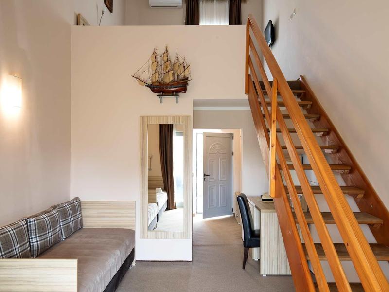 Wohnzimmer mit Holztreppe, kleinem Sofa, Schreibtisch und Wandspiegel mit Schiffsmodell.