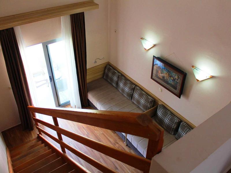 Blick von Treppe auf helles Wohnzimmer mit braunen Gardinen, Sofa und Kunstbild an weißer Wand.