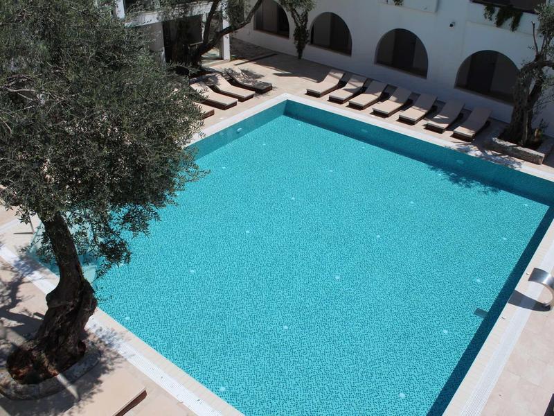 Großer, rechteckiger Pool mit klar blauem Wasser, umgeben von Liegestühlen und Bäumen.