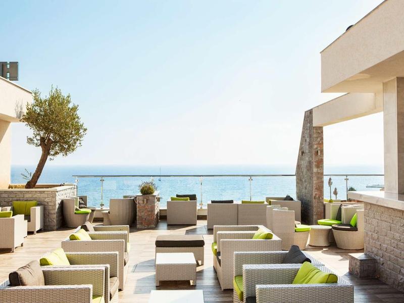Moderner Außenbereich mit Sitzmöbeln und Blick auf das blaue Meer unter klarem Himmel.