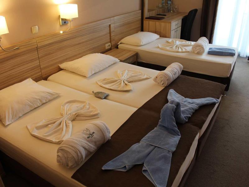 Drei Betten im Hotelzimmer, jeweils mit weißen Handtüchern kunstvoll gefaltet und brauner Tagesdecke.