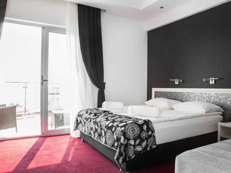 Modernes Schlafzimmer mit großem Bett, schwarzer Wand, rotem Teppich und Balkon mit Glasfenstern.