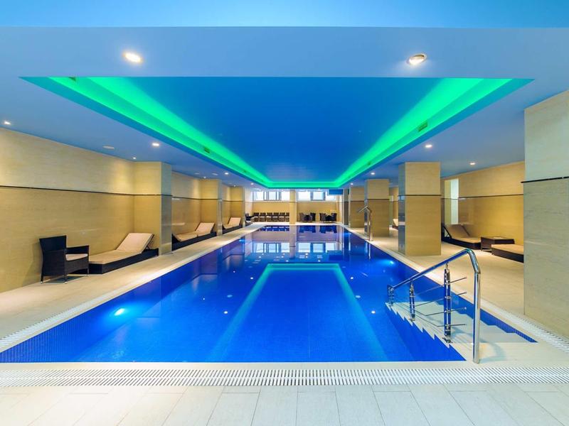 Ein großer Innenpool mit blauem Wasser, bequemen Stühlen und grün-blauer Deckenbeleuchtung.