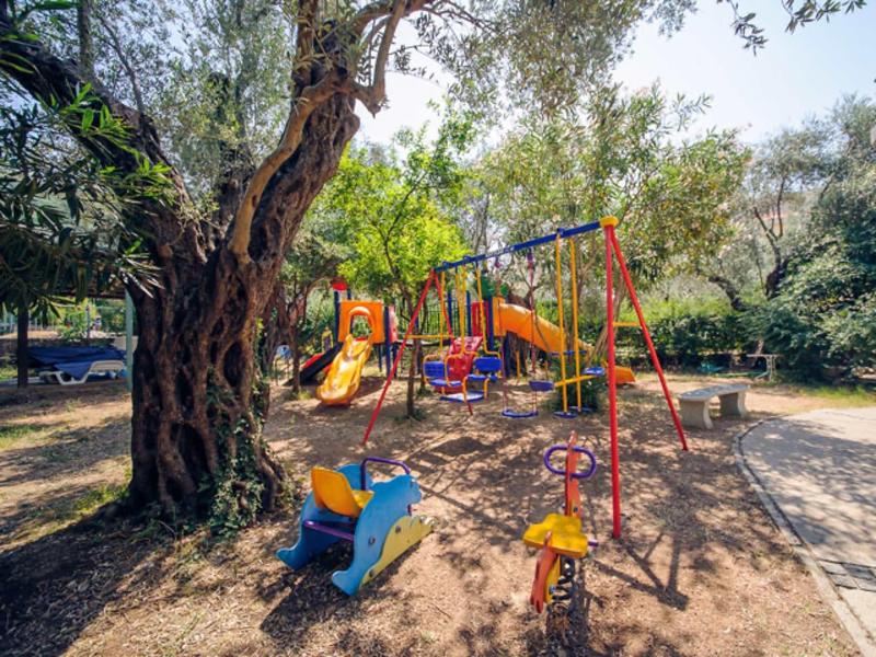 Kinderspielplatz mit bunten Rutschen, Schaukeln und Klettergeräten unter großen Bäumen.