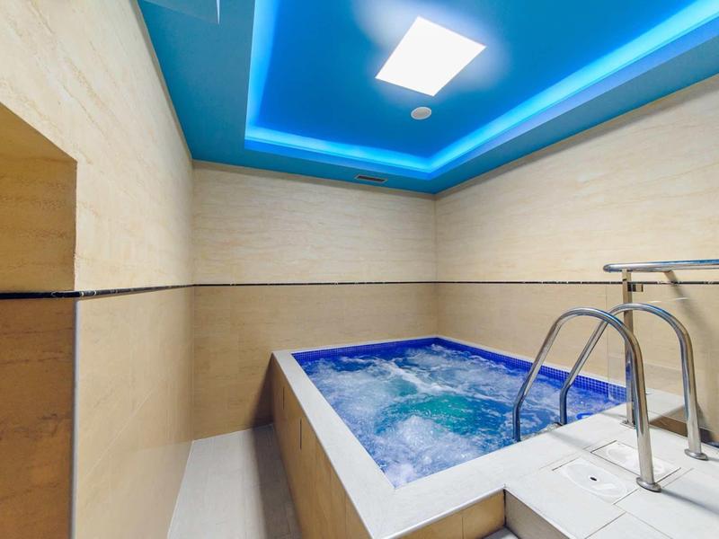Moderner Whirlpool mit klaren Linien, blauer LED-Decke und beiger Wandverkleidung.