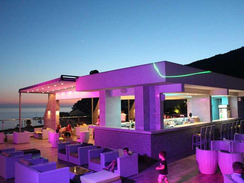 Moderner Außenbereich mit Bar, Sitzgelegenheiten und rosa-lila Beleuchtung bei Dämmerung.