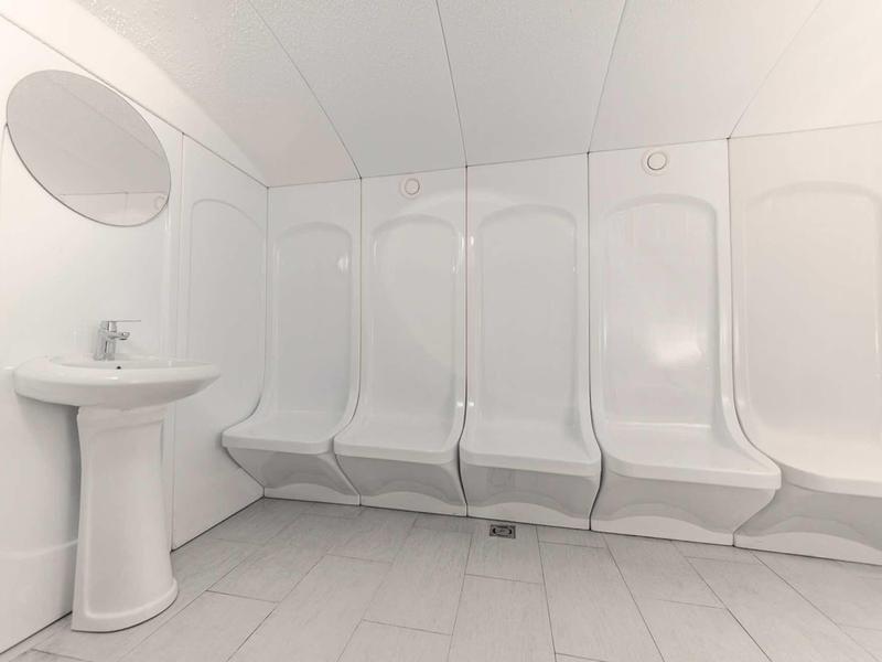 Weißer Duschraum mit mehreren Duschen nebeneinander und einem weißen Waschbecken links.