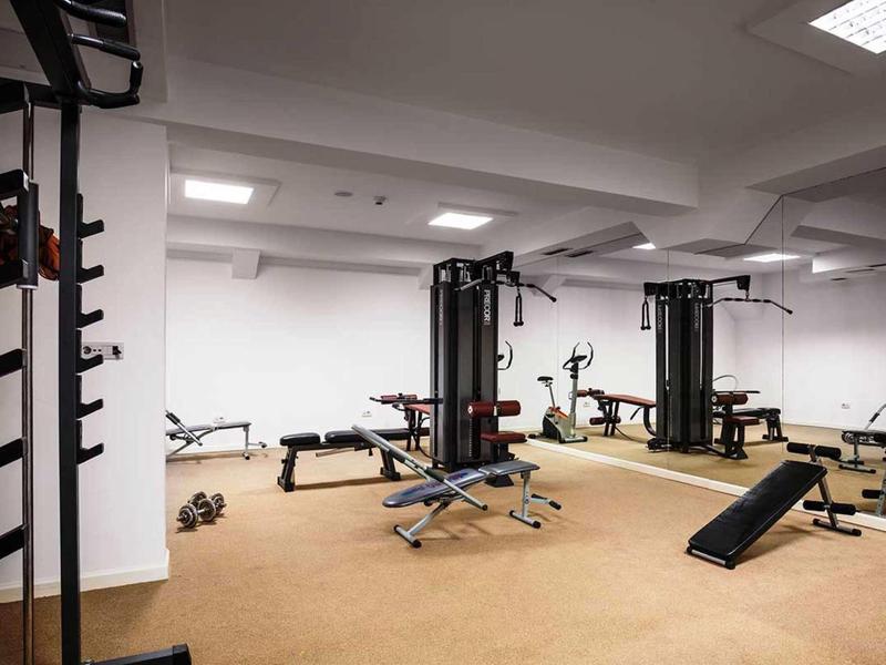 Großer, heller Fitnessraum mit verschiedenen Trainingsgeräten und hellbraunem Bodenbelag.