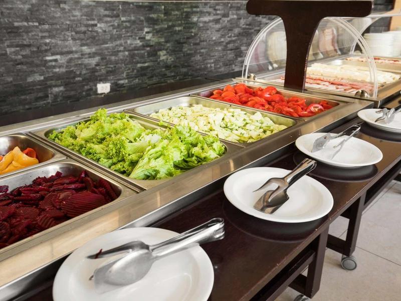 Buffet mit frischem Salat, Tomaten, Gurken und Rote Bete in Metallbehältern neben Tellern.