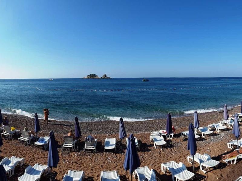 Strand mit blau-weißen Sonnenschirmen und Liegestühlen unter klarem Himmel am Meerufer.