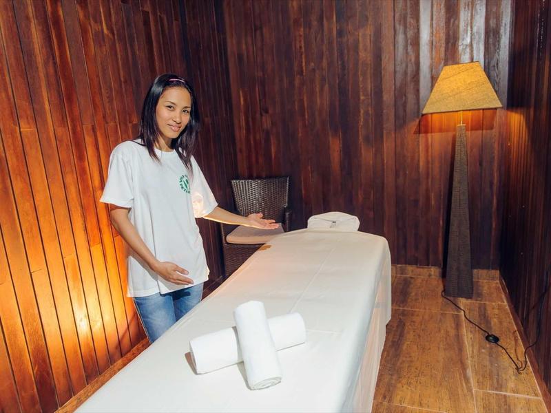 Eine Frau bereitet in einem gemütlichen Holzzimmer eine weiße Massageliege vor.