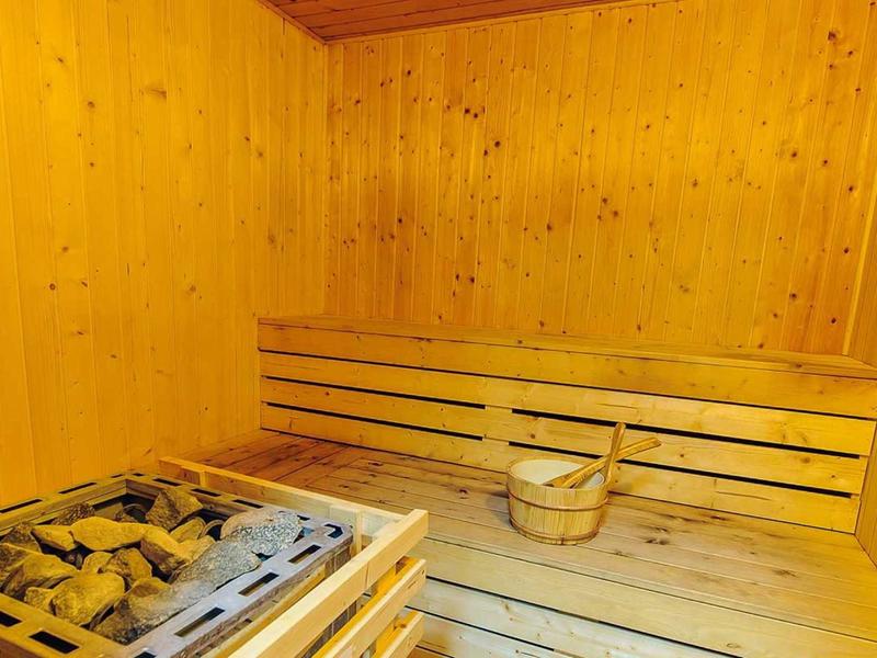 Holzsauna mit Holzbänken, Saunaofen mit Steinen und Holzeimer mit Schöpflöffel.
