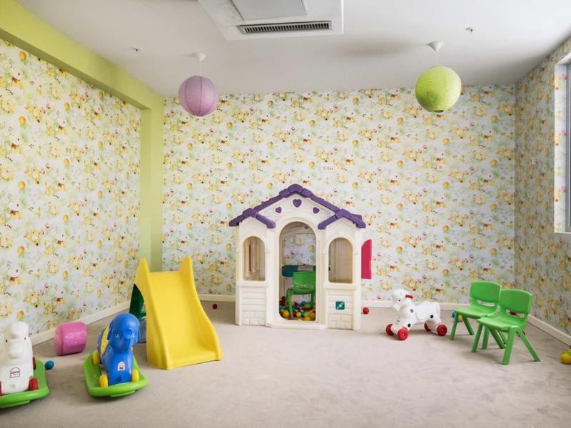 Kinderspielzimmer mit buntem Spielhaus, gelber Rutsche und verschiedenen Spielzeugen auf beige Teppich.
