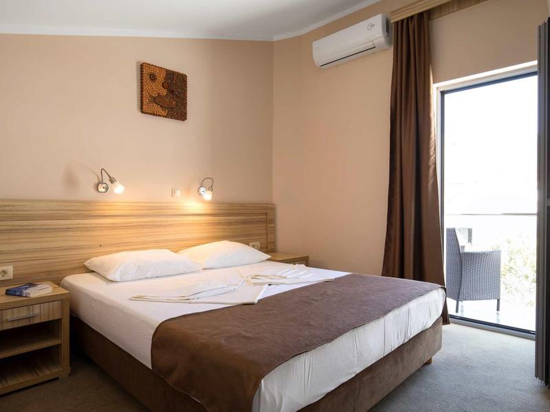 Hell eingerichtetes Schlafzimmer mit Doppelbett, Nachttisch, Klimaanlage und Balkon mit Blick nach draußen.