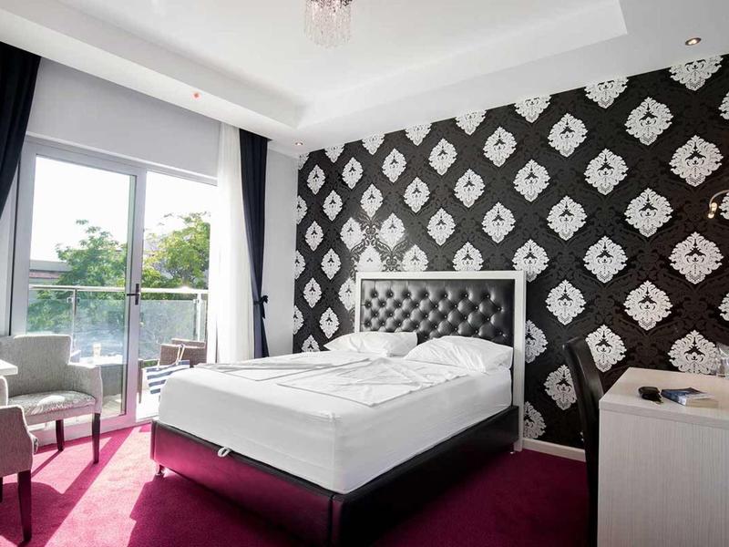 Modernes Schlafzimmer mit weißen Möbeln, schwarzer Tapete, rotem Teppich und Balkon mit Glasfenstern.