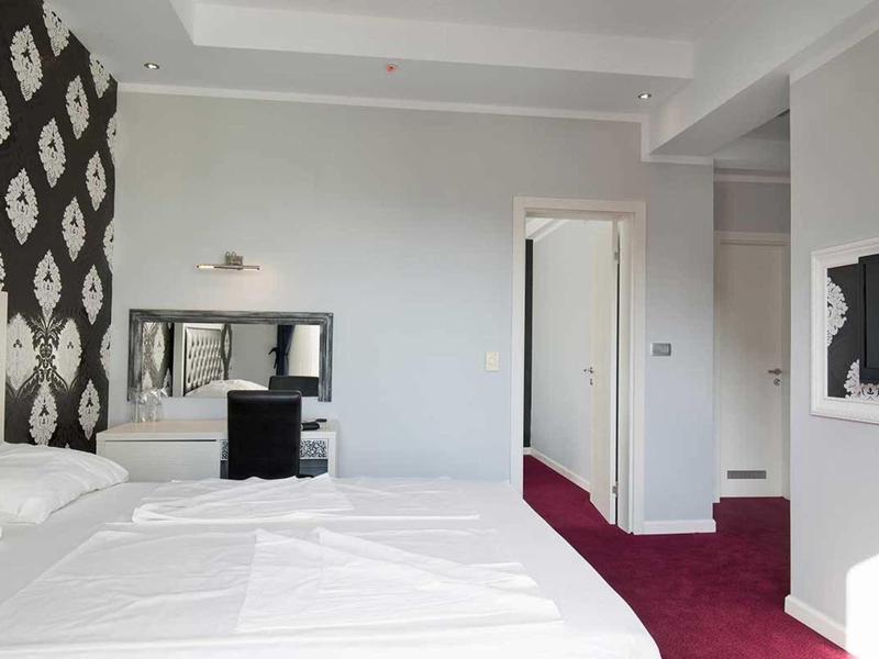 Modernes Schlafzimmer mit weißem Bett, rotem Teppich und schwarzem Schreibtisch vor großem Spiegel.