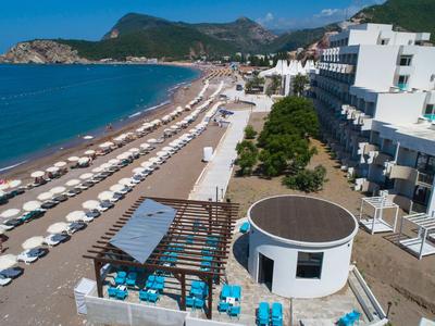 Vue sur une longue plage de sable avec parasols et un bâtiment d'hôtel blanc au bord de la mer.