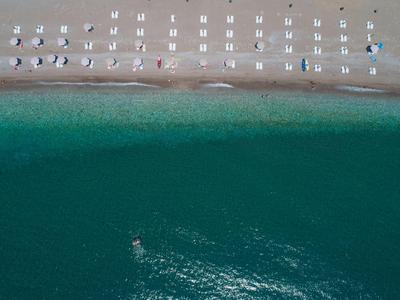 Vue drone d'une plage avec chaises longues et parasols au bord et eau turquoise.