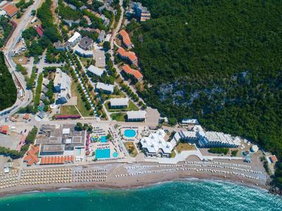 Luftaufnahme eines Küstenresorts mit Pool, Strand voller Liegestühle und dichtem Wald im Hintergrund.