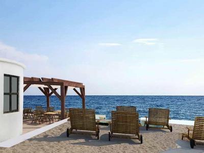 Plage avec des chaises longues en bois devant un bâtiment blanc rond sous un ciel bleu et la mer en arrière-plan