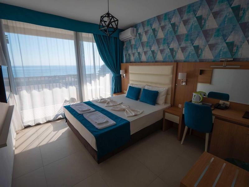 Helles Schlafzimmer mit Doppelbett, blau-weißer Bettwäsche, Fenster mit Meerblick und Schreibtisch.