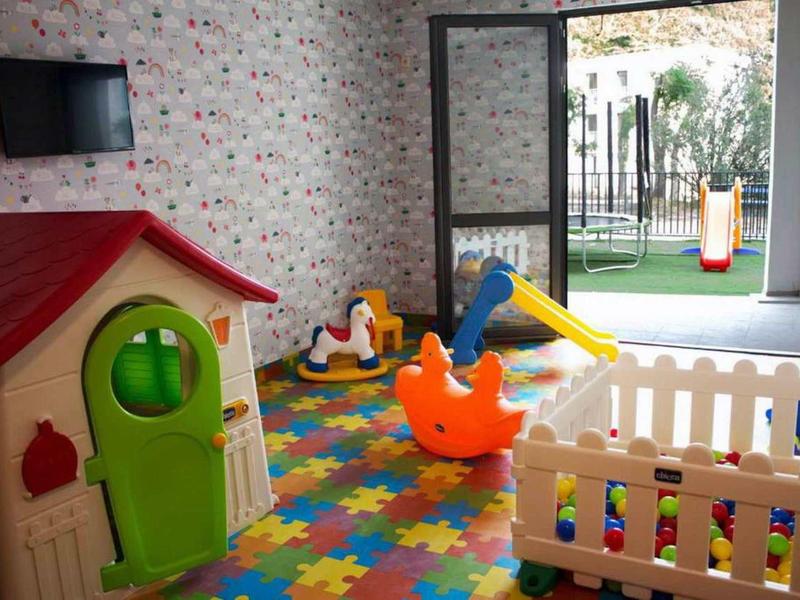 Bunter Kinderspielraum mit Spielhaus, Rutsche, Schaukeltier und gepuzzeltetem Bodenbelag.