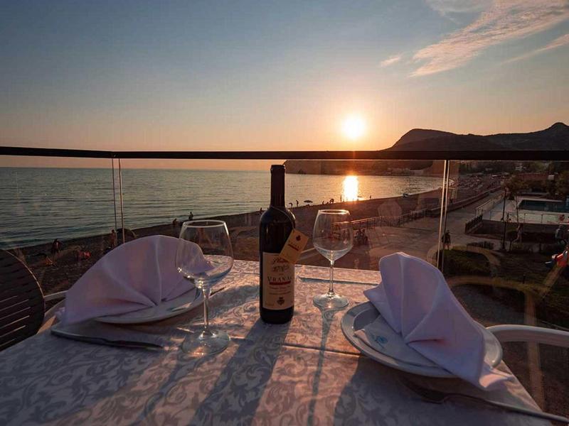 Zwei gedeckte Teller mit Servietten und eine Weinflasche auf einem Tisch am Meer bei Sonnenuntergang.