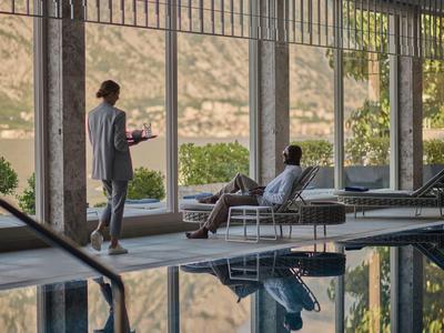 Elegantní muž podává nápoje u bazénu s výhledem na hory a jezero.