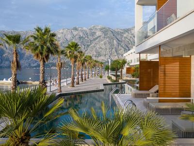 Moderne Hotelterrasse mit Pool, Palmen und Berglandschaft im Hintergrund.