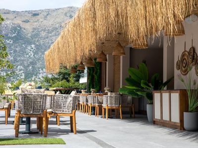 Außenbereich eines Restaurants mit Strohdach, Holztischen und Aussicht auf Berge.