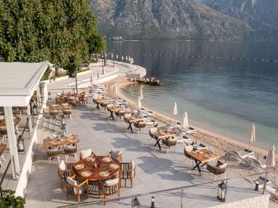 Terrasse mit Tischen und Stühlen am Strand mit Blick auf das Meer und Berge im Hintergrund.