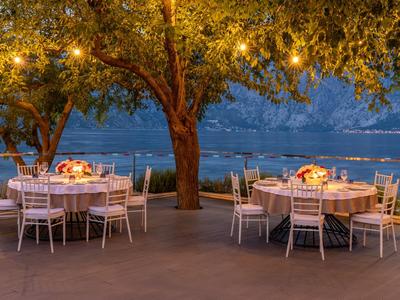 Abendliche Außenterrasse mit gedeckten Tischen und beleuchteten Bäumen am Wasser.