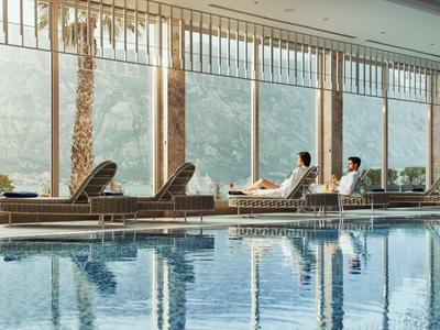 Innenpool mit Liegestühlen und großen Fenstern mit Blick auf Bäume und Berge.
