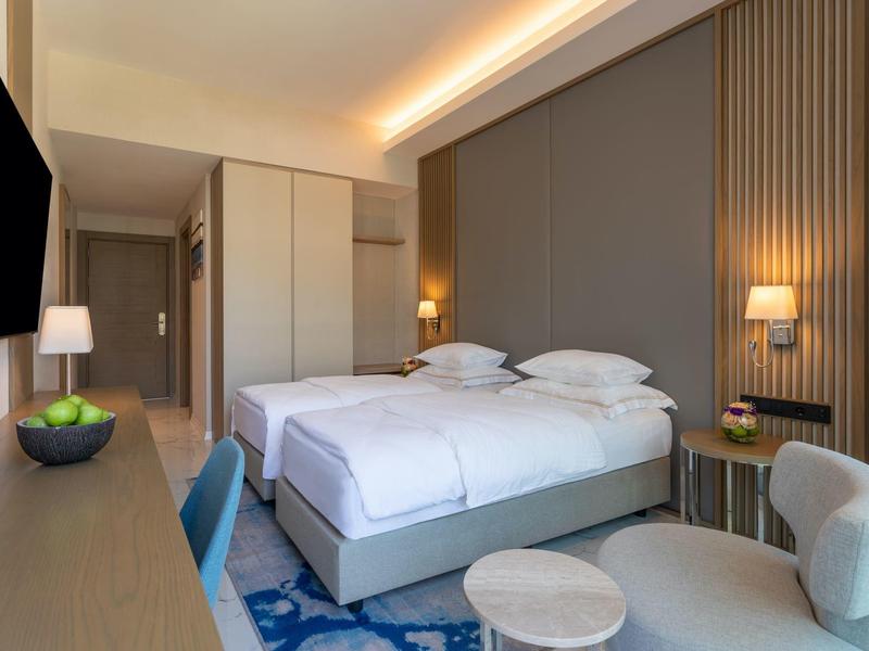 Moderní hotelový pokoj se dvěma jednolůžky, psacím stolem, TV a posezením.