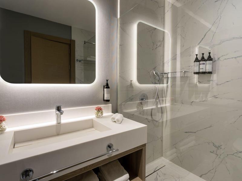 Moderní koupelna se svítícím zrcadlem, umyvadlem a sprchou s prosklenou stěnou.