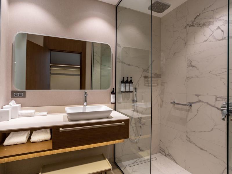 Moderní koupelna s umyvadlem, zrcadlem a skleněnými dveřmi do sprchy s mramorovým efektem.