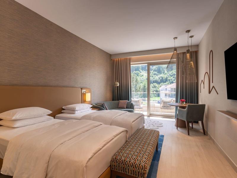 Moderní hotelový pokoj se dvěma jednolůžky, balkonem a posezením s výhledem ven.