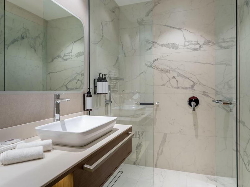 Moderní koupelna s mramorovými stěnami, umyvadlem na desce a dešťovou sprchou