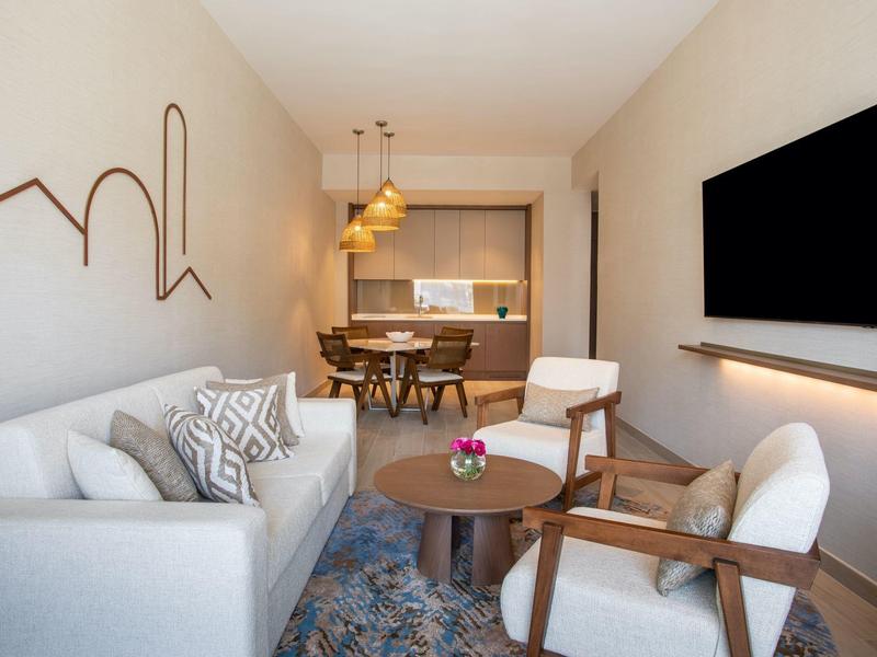 Moderně zařízený obývací pokoj s pohovkou, křesly, konferenčním stolkem a nástěnnou dekorací v neutrálních barvách.