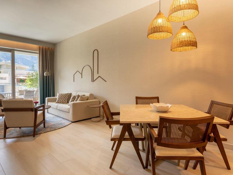 Moderně zařízený obývací pokoj s jídelním koutem, pohovkou, křesly a velkými okny s výhledem ven.