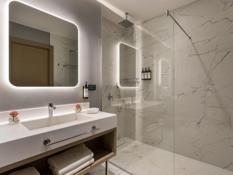 Moderní koupelna se osvětleným zrcadlem, dvojumyvadlem a sprchou s prosklenou stěnou.