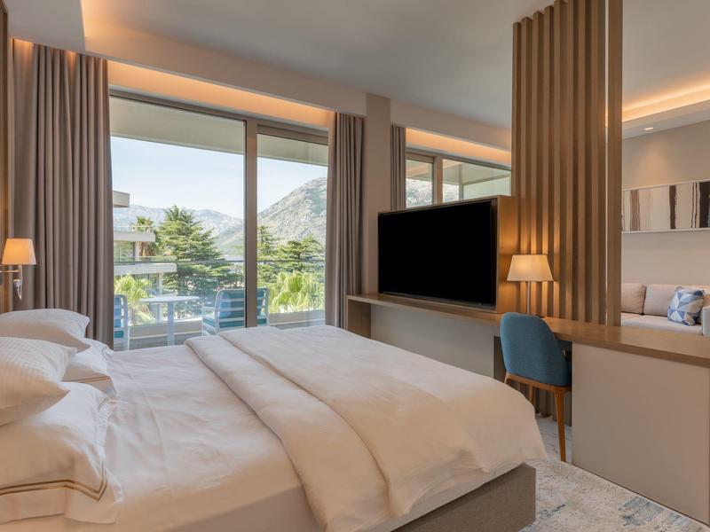 Moderní hotelový pokoj s velkou postelí, televizí a balkonem s výhledem na hory.