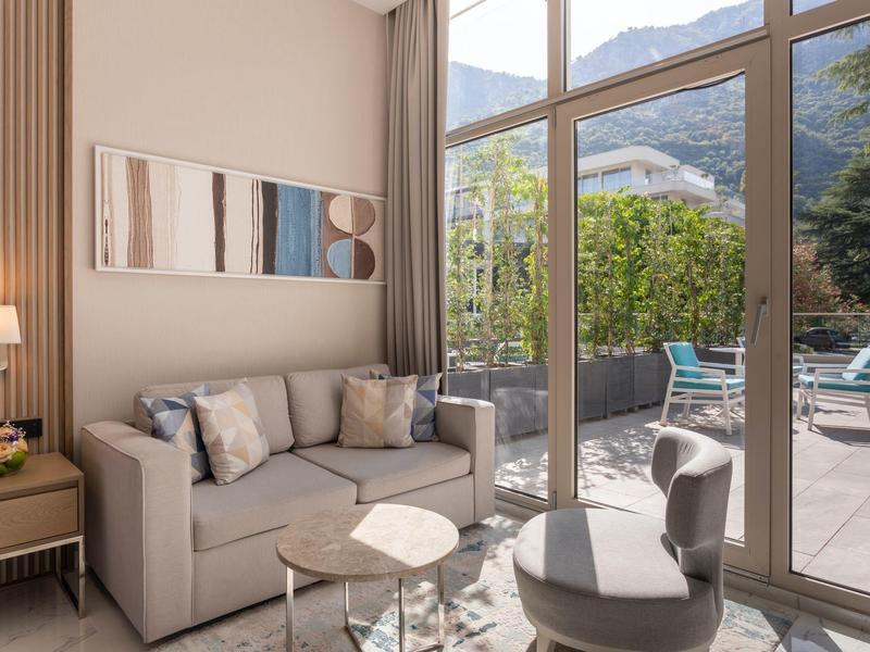 Světý pokoj hotelu s pohovkou, židlemi a velkými prosklenými dveřmi na terasu s výhledem na hory.