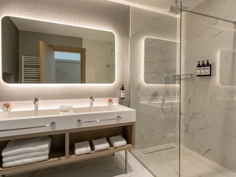 Moderní koupelna se osvětleným zrcadlem, dvojitým umyvadlem a sprchovým koutem.