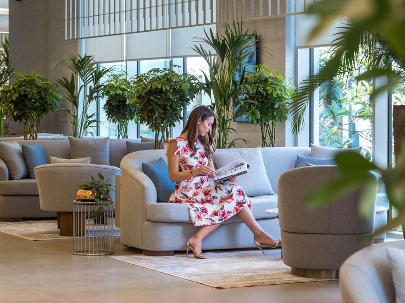 Žena sedí v moderní hotelové hale na pohodlné pohovce a čte.