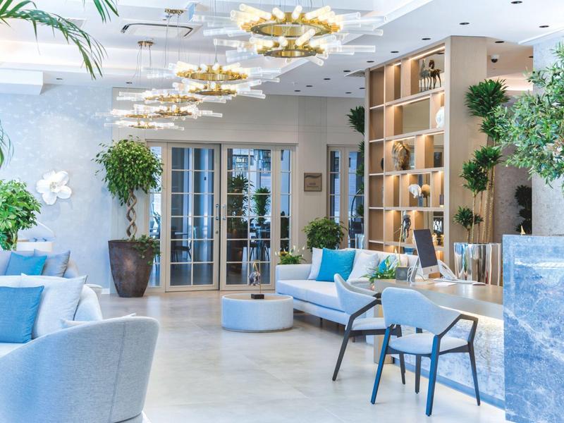 Svítivá, moderní hotelová hala s posezením, rostlinami a dekorativními stropními světly.