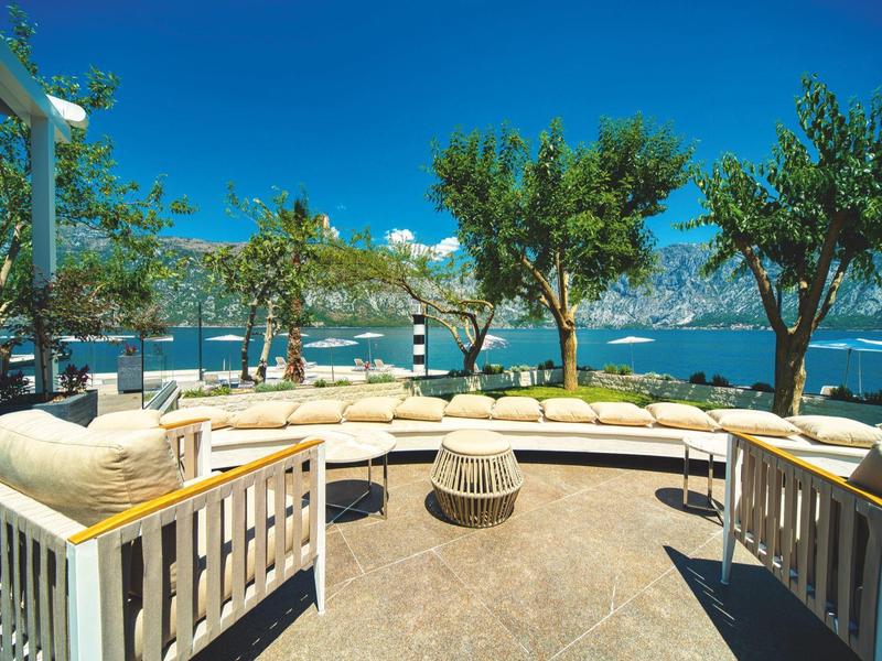 Venkovní posezení s bílými pohovkami s výhledem na moře a stromy