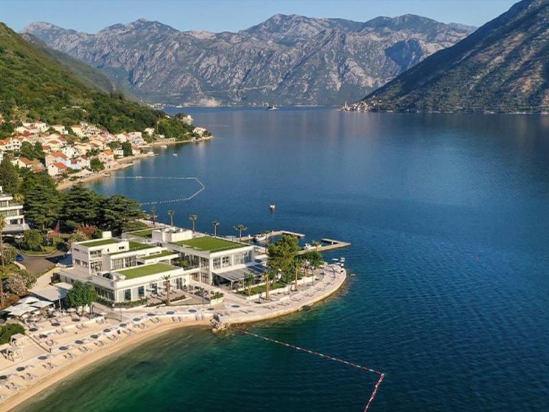 Zátoka s čistou vodou obklopená horami a malou přímořskou vesnicí s pláží a hotely.