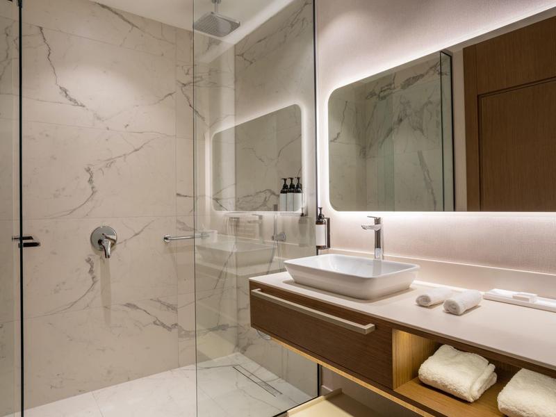 Moderní koupelna s mramorovými stěnami, skleněnou sprchou a osvětleným zrcadlem